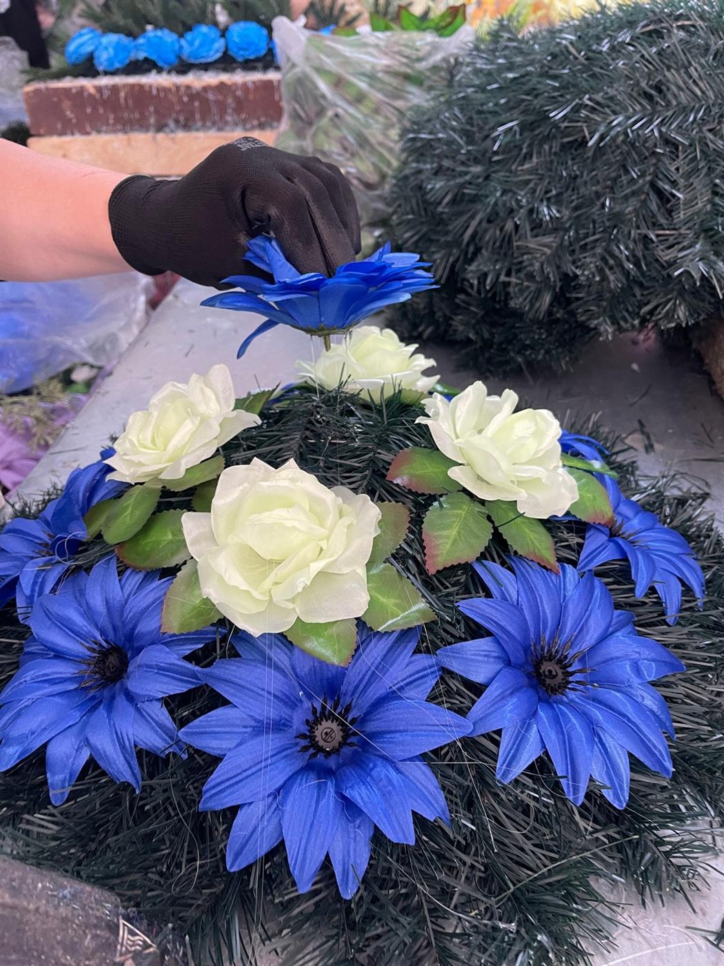 Coroană funerară artificială în lucru, cu flori albastre și trandafiri albi